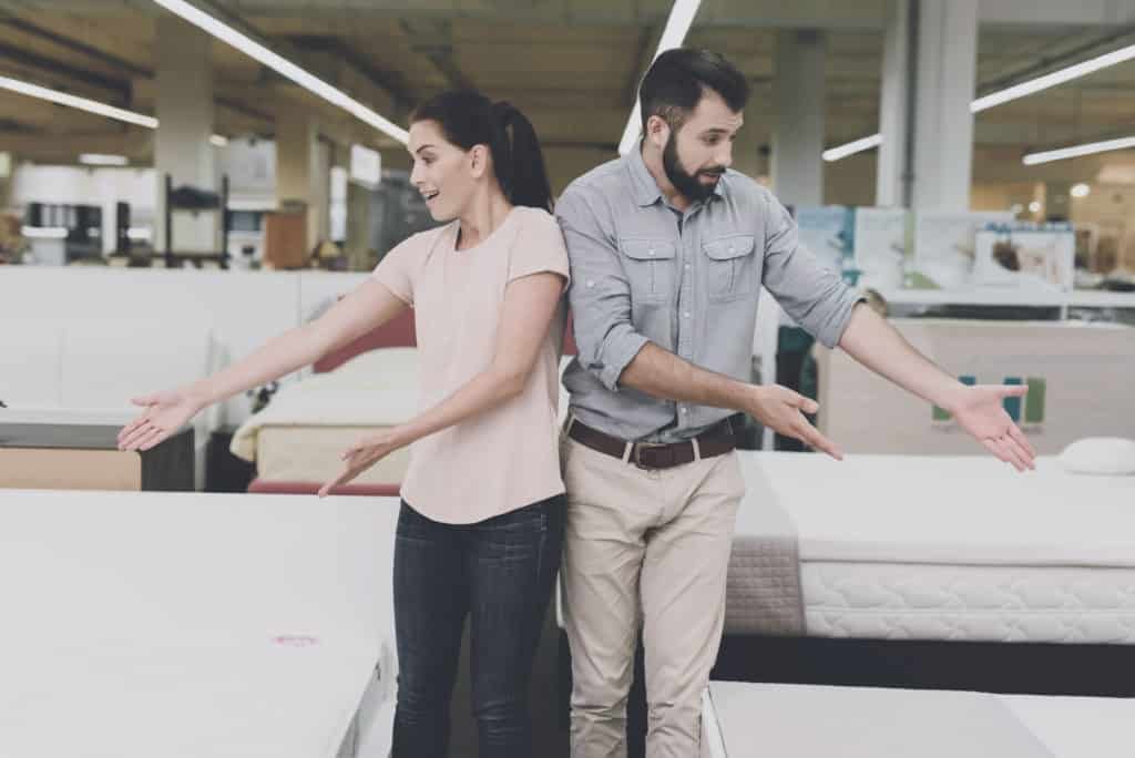 A couple chooses a mattress in the store. A man points to one, a woman to another